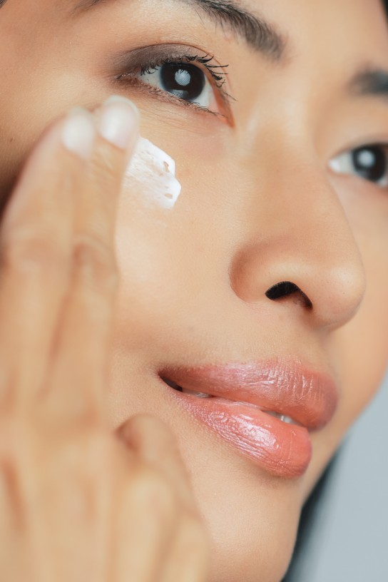 Beautiful Asian Woman Gently Touching Her Face, Looking Away. Young Adult Female with Lush Black Hair Makes Her Skin Soft, Clean with Natural Cosmetics Skincare Product. Close-up Portrait