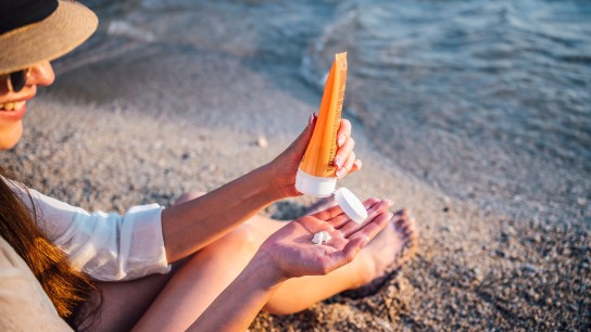 Young cheerful woman using sunscreen cream on the beach