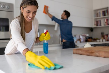 Happy Latin American couple at home cleaning the kitchen - domestic life concepts