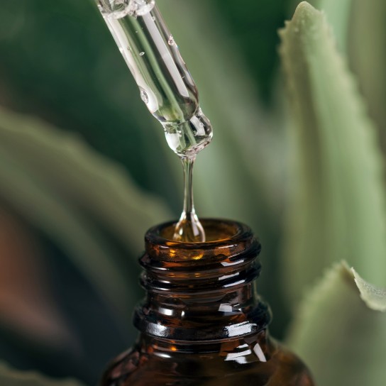 Close-up of a pipette dripping into a bottle. Dropper with hyaluronic liquid or essential oil. Liquid drips into a bottle on a blurred nature background