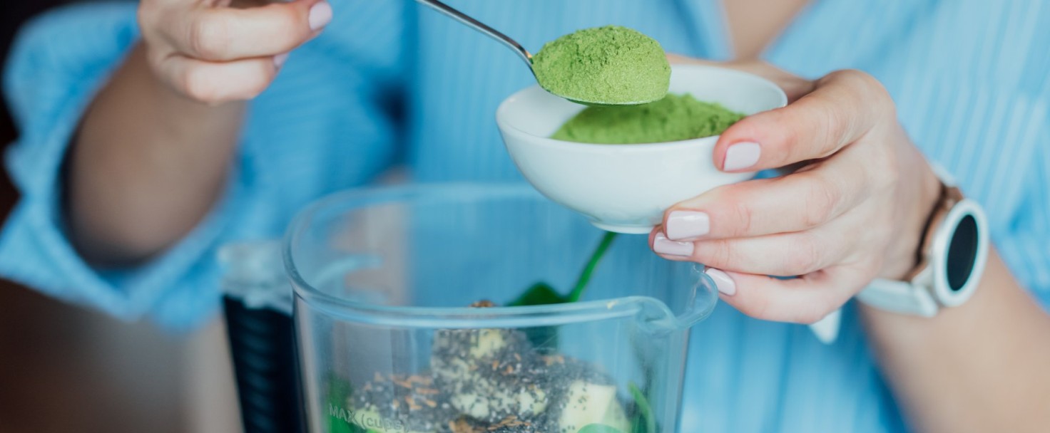 Close up woman adding wheat grass green powder during making smoothie on the kitchen. Superfood supplement. Healthy detox vegan diet. Healthy dieting eating, weight loss program. Selective focus.