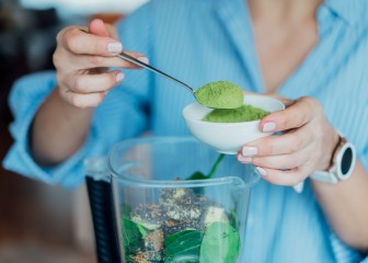 Close up woman adding wheat grass green powder during making smoothie on the kitchen. Superfood supplement. Healthy detox vegan diet. Healthy dieting eating, weight loss program. Selective focus.