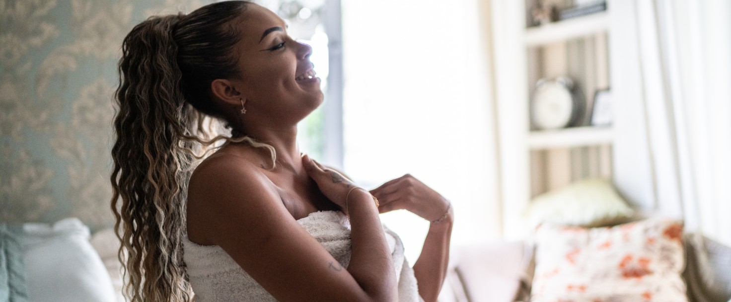 Young woman applying moisturizer on the body at home