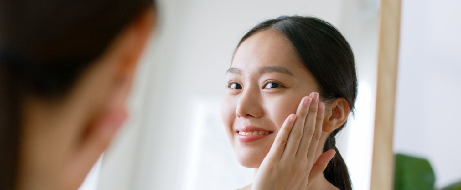 Young Asian beautiful woman touching healthy facial skin look at mirror, Asian beauty skin concept