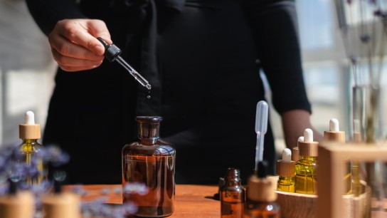 Woman preparing aromatic liquid for diffuser or perfume from essential flower oil. DIY. Many bottles and jars with different types of oils, lavender flowers and essences. The process of creating perfume, workshop