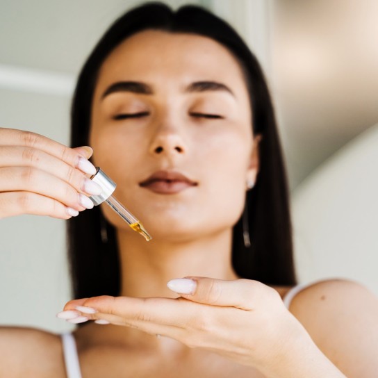 Girl with hyaluronic acid or serum pipette in hands close-up. Young woman is applying moisturizing serum on skin