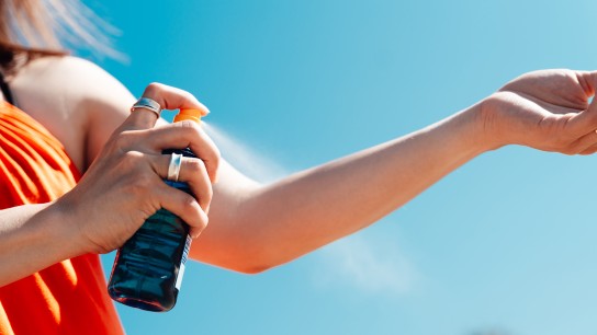 Cropped shot of young woman putting sunscreen lotion on her body while sunbathing on the beach. Summer vacation.