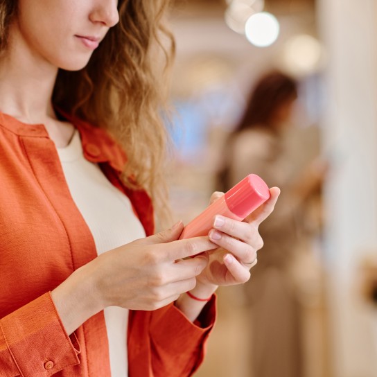 Close-up of young woman choosing cream for bodycare standing in the store