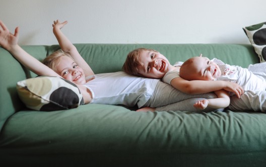 Three emotional sibling children together on green sofa at home. Sincere authentic photo and copy space.