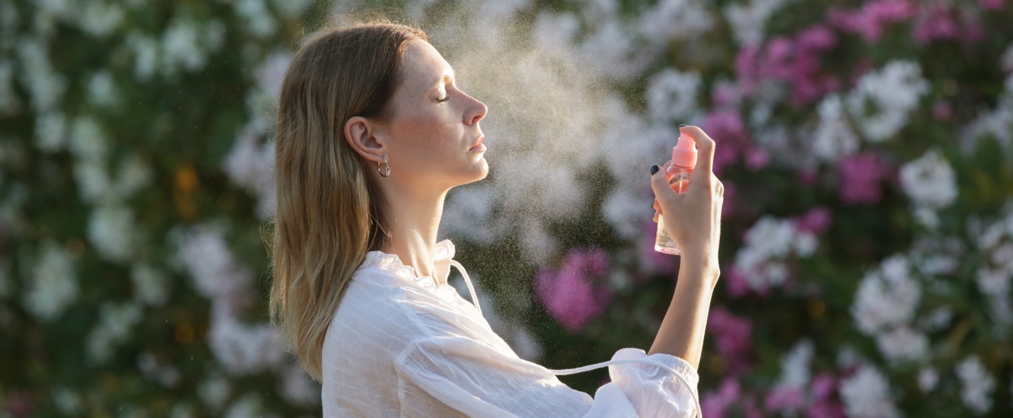 Woman spraying facial mist on her face, summertime skincare concept