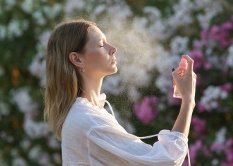 Woman spraying facial mist on her face, summertime skincare concept