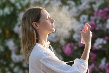 Woman spraying facial mist on her face, summertime skincare concept