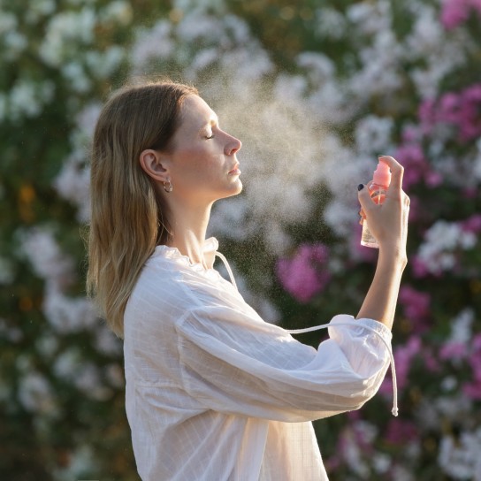 Woman spraying facial mist on her face, summertime skincare concept