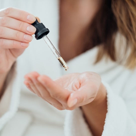 Woman drips cosmetic oil onto her palm to massage her scalp and improve the quality and beauty of her hair