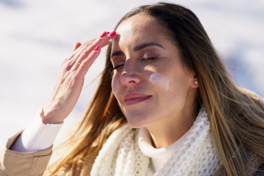 Smiling woman with eyes closed applying sunscreen in winter