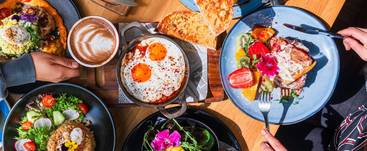 Table top view of breakfast food displayed on table, people eating food.