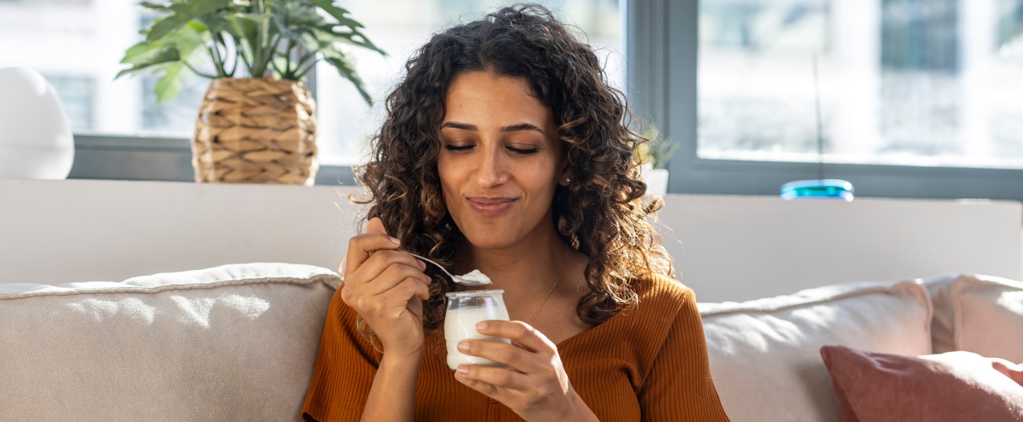 Smiling woman eating yogurt on sofa at home
