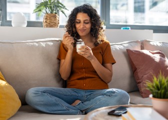 Smiling woman eating yogurt on sofa at home