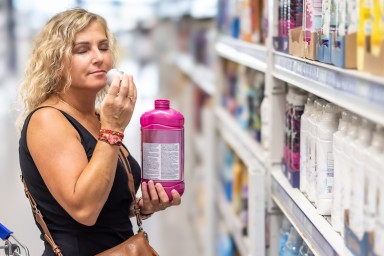 A woman smiles and smells the cap of a bottle of fabric softener. A satisfied customer is shopping in a drugstore