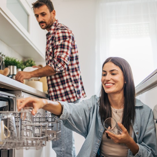Young cheerful couple loading the dishwasher in the kitchen.