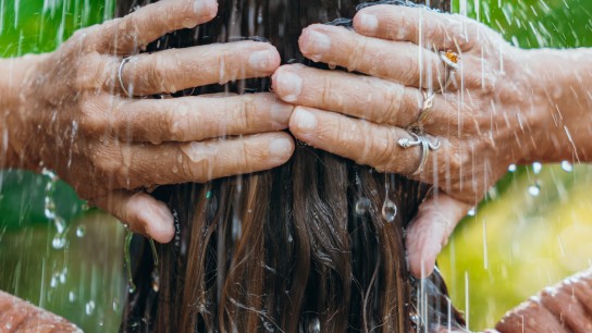 Woman with wet hair stands under a garden shower. Relaxing in a tropical setting, surrounded by lush greenery. Outdoor tranquility in a natural environment.