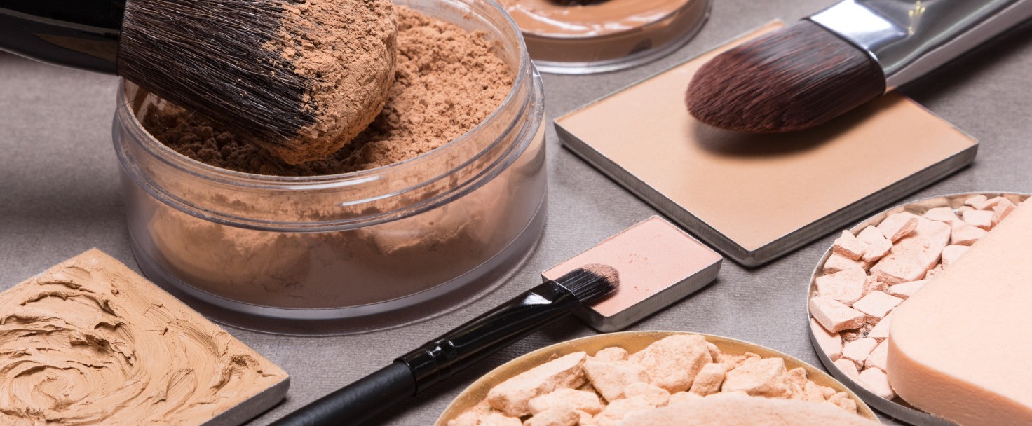 Makeup products and accessories to even out skin tone and complexion: loose and compact powders, concealer pencil, correctors, liquid foundation with brushes and cosmetic sponges on textured surface