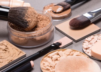 Makeup products and accessories to even out skin tone and complexion: loose and compact powders, concealer pencil, correctors, liquid foundation with brushes and cosmetic sponges on textured surface