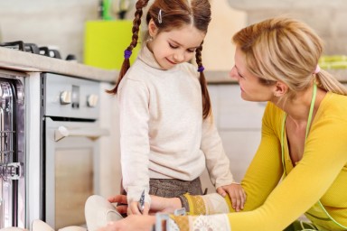 Smiling mother and daughter using dishwasher in the kitchen.