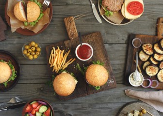 Different food on a wooden table, burgers, fries, grilled eggplant, salad, different sauces and olives, top view. Outdoors food Concept