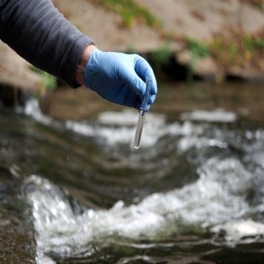 Water sample. Gloved hand into the water collecting tube. Analysis of water purity, environment, ecology - concept. Water testing for infections, harmful emissionsWater sample. Gloved hand into the water collecting tube. Analysis of water purity, environment, ecology - concept. Water testing for infections, harmful emissions