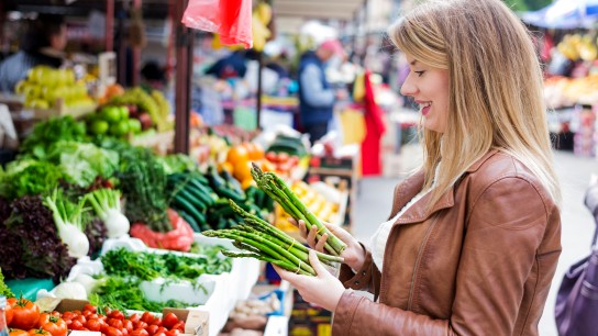 Portrait of Happy Vegetarian Girl customer holding Fresh green asparagus in grocery store, green grocery and traditional local goods, female vegetable market during the day.