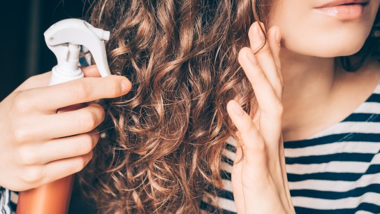 Woman applying spray on curly brown hair close-up