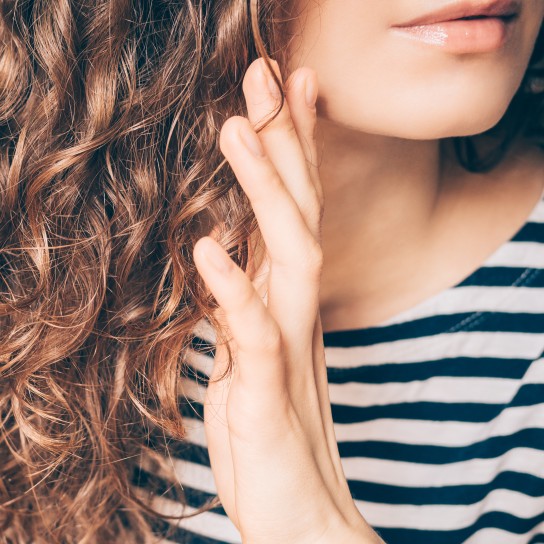 Woman applying spray on curly brown hair close-up