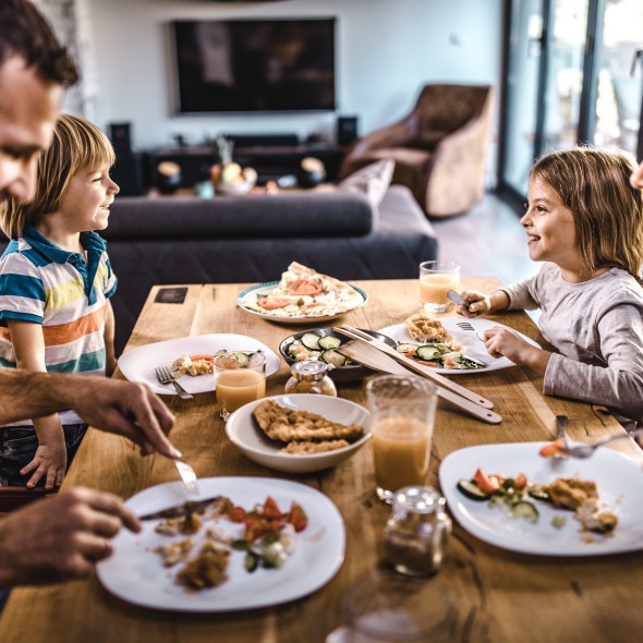 Happy family communicating during lunch time in dining room. Focus is on kids.