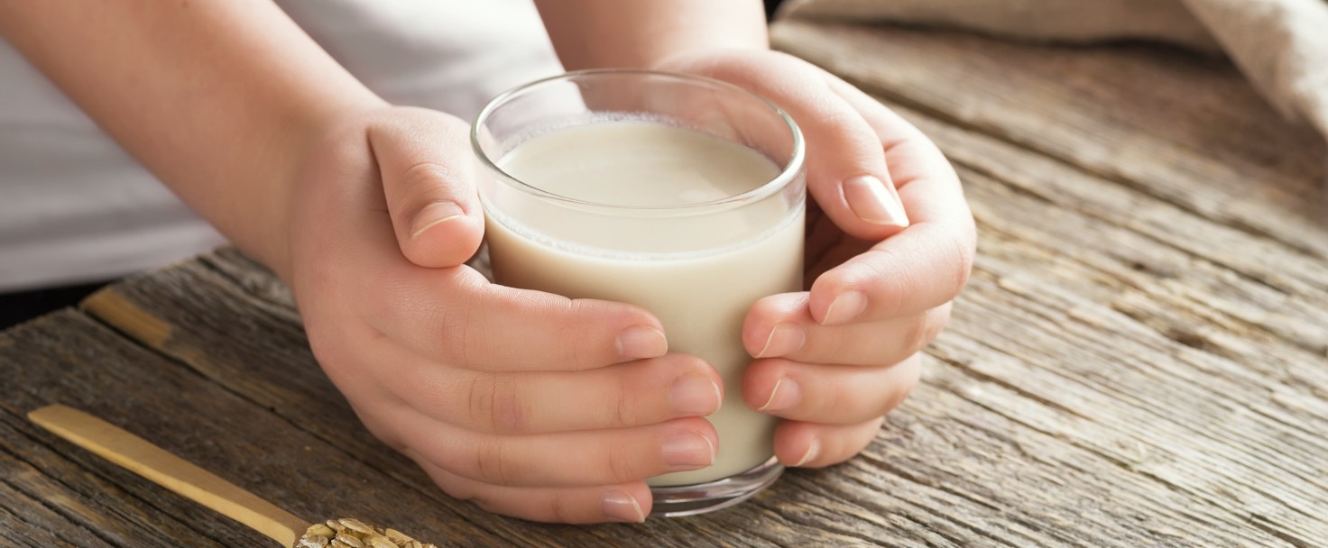 Young adult hands holds drinking glass with organic oat milk . Healthy eating lactose free milk substitute concept .Close up,selective focus.