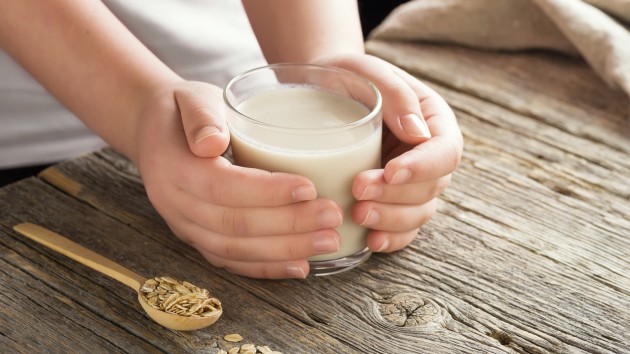 Young adult hands holds drinking glass with organic oat milk . Healthy eating lactose free milk substitute concept .Close up,selective focus.