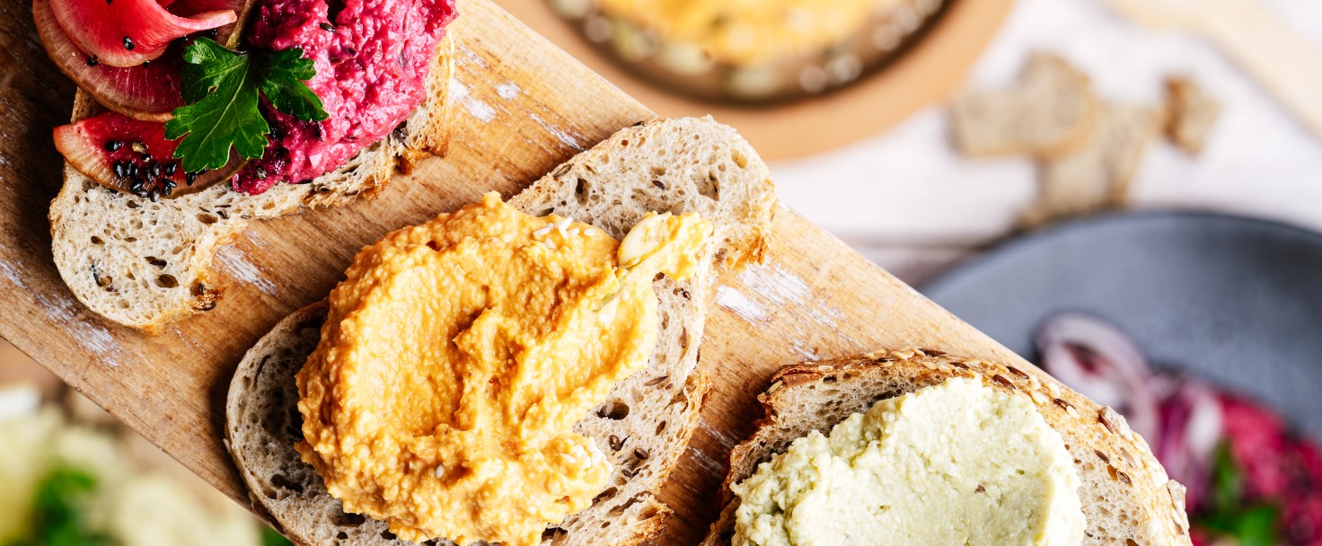 Eating healthy vegan snacks, gourmet sandwiches variety. Hummus with wakame seaweed, roasted red bell pepper, beetroot on cutting board viewed from above, personal perspective, plant based food
