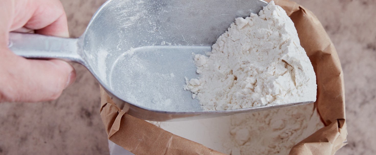 White flour on flour shovel. Opened bag on brownish surface. High point of view.