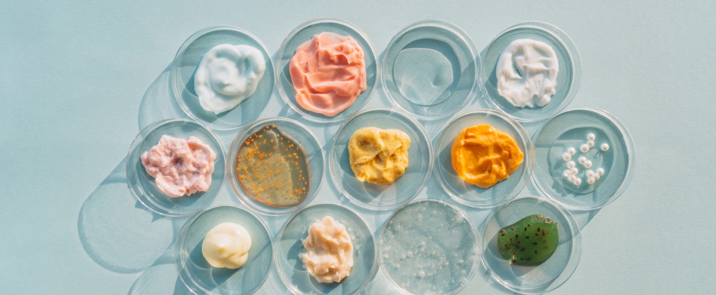Multicolored creams, scrubs, face serums and gels in many Petri dishes on light blue background. Concept of cosmetics laboratory researches. Photography in flat lay style