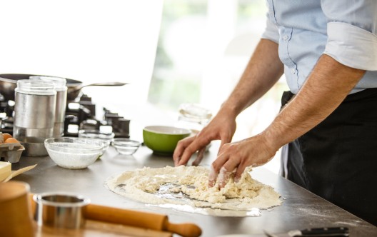 Mid adult man with black apron baking pizza dough in the kitchen.