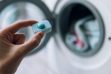 Close up of hand holding detergent capsule in front of washing machine
GettyImages-1332295340.jpg
