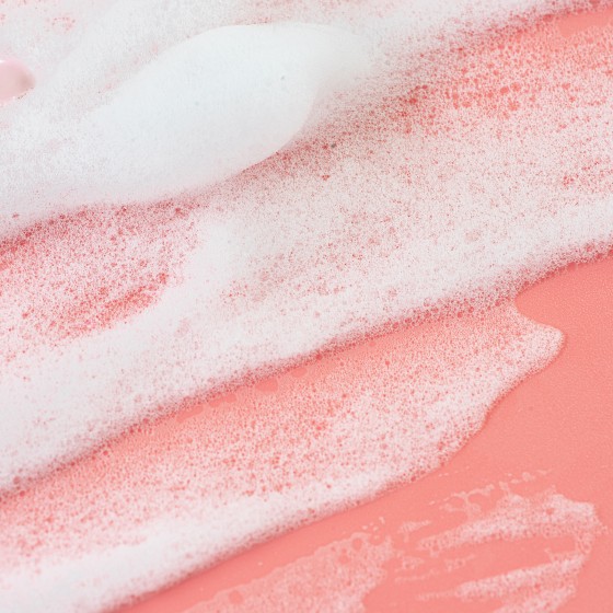 Smears of White Foam Soap or Cosmetic Milk or Beauty Foam on pastel pink coral rose color background.  Texture of white foam. Concept of home facial cleanser in selfcare routine and healthy lifestyle. Flat lay. Close-up. Copy space.