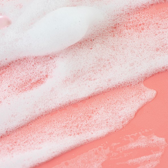 Smears of White Foam Soap or Cosmetic Milk or Beauty Foam on pastel pink coral rose color background.  Texture of white foam. Concept of home facial cleanser in selfcare routine and healthy lifestyle. Flat lay. Close-up. Copy space.