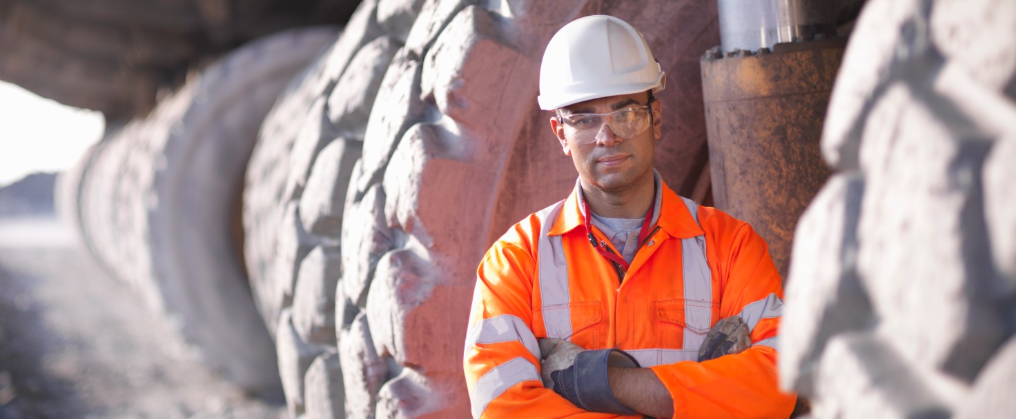 Portrait-of-miner-standing-next-to-dumper-truck-tyresin-open-cast-coalmine