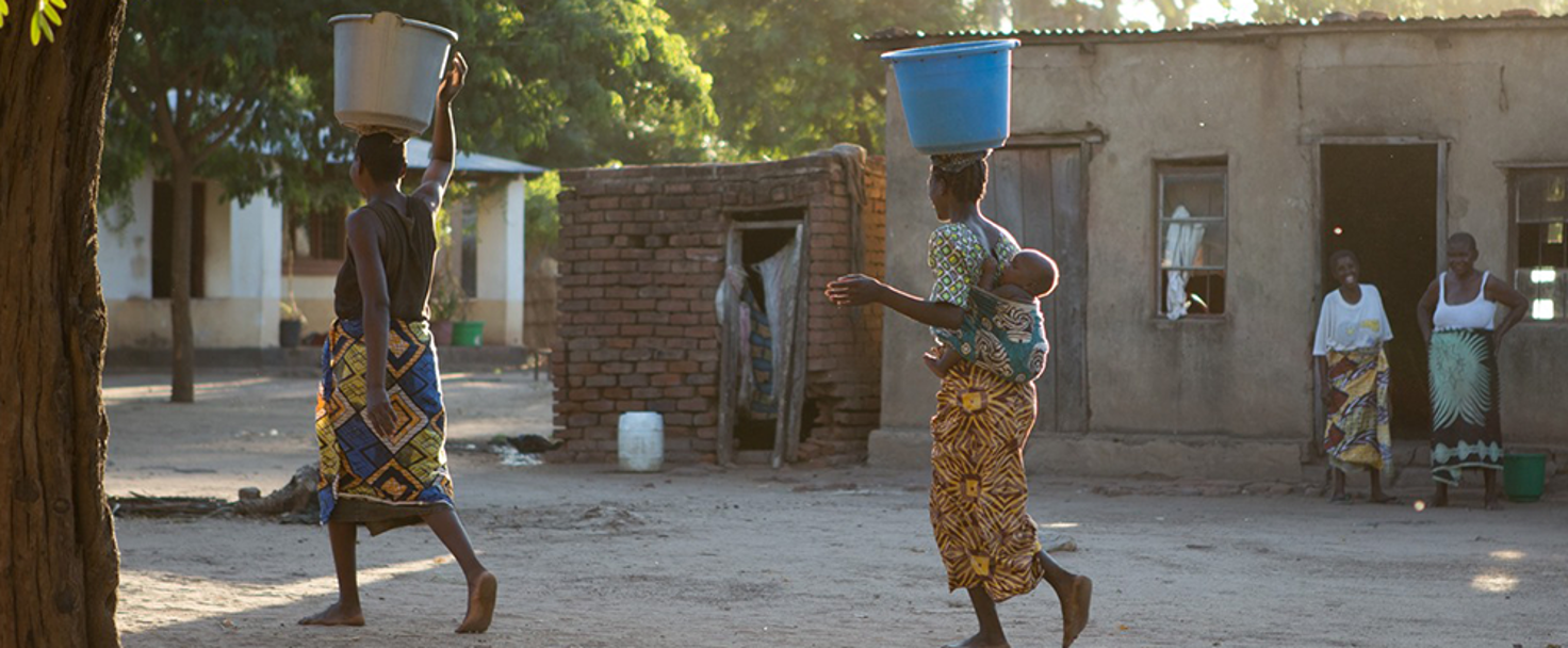 Women carrying water on their heads in large tubs
