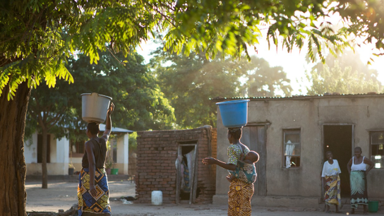 Women carrying water on their heads in large tubs