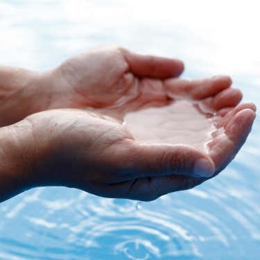 Hands in cupped form getting water from a lake or fountain