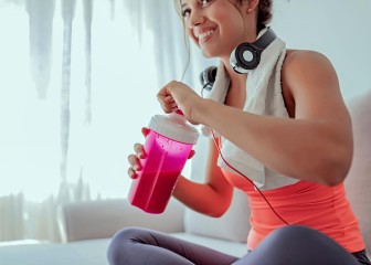 Close up Image of Young Fitness Woman With Headphones Drink Protein Shake While Sitting in Her Living Room After Workout. Young sporty woman athlete in sportswear sitting, drinking protein cocktail from shake
GettyImages-1043755718.jpg