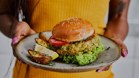 Žena drží zdravý veganský hamburger z cukety, zeleného hrášku, koření, bylinek a koření na ručně vyrobeném keramickém talíři, záběr zblízka