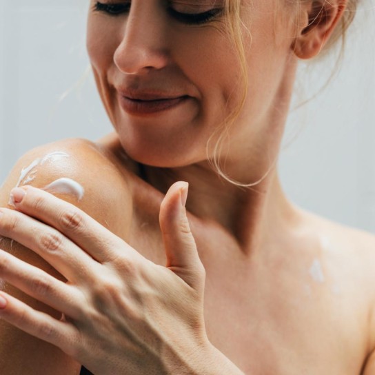 Close up shot of a blonde woman in her 30s wrapped in a towel, applying body lotion.
GettyImages-1400481169.jpg